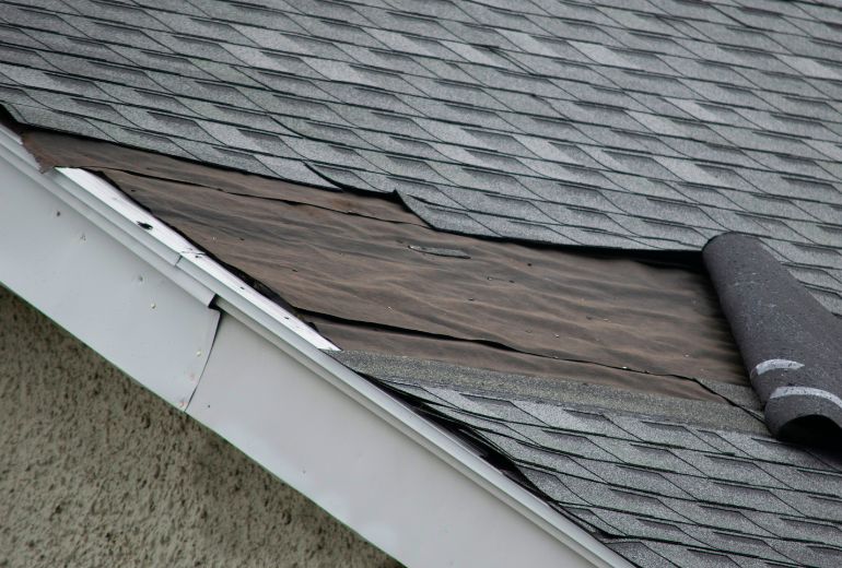 Damaged shingles lifted on a roof, revealing potential vulnerabilities and the need for maintenance.